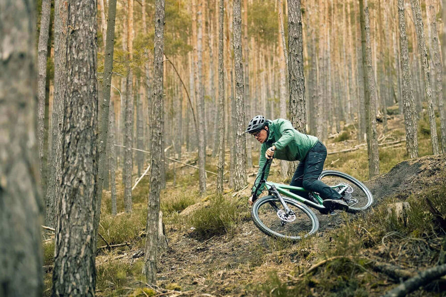 Ein Mann fährt mit dem Fahrrad im Wald - Men's BUEX Pro 2.0. Robuste MTB Hose aus hochelastischem 4-Wege-Stretch-Material. Hergestellt aus Bio-Nylon auf Basis von Rizinus-Öl. Extrem abriebfest. Dynamischer, bewegungsoptimierter Schnitt. Breiter Bund für sicheren Halt. Gürtelschlaufen. 2 Taschen vorne. 1 Zip-Tasche am Bein. Vorgeformte Kniepartie für Protektoren. Gelaserte Belüftungsöffnungen am Knie hinten. Reflektierende Elemente. TRIPLE2 - Nachhaltige Radbekleidung aus dem Norden.