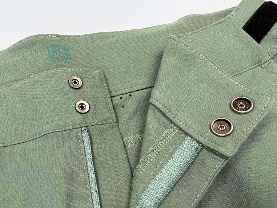 Eine Nahaufnahme einer grünen Jacke für Männer - BUEX Pro 2.0. Hochwertiges, abriebfestes Material aus Bio-Nylon auf Basis von Rizinus-Öl. Dynamischer Schnitt, breiter Bund, Gürtelschlaufen, 2 Taschen vorne, 1 Zip-Tasche am Bein, vorgeformte Kniepartie für Protektoren, Belüftungsöffnungen am Knie, reflektierende Elemente. Robuste MTB Hose für jeden Einsatzbereich.